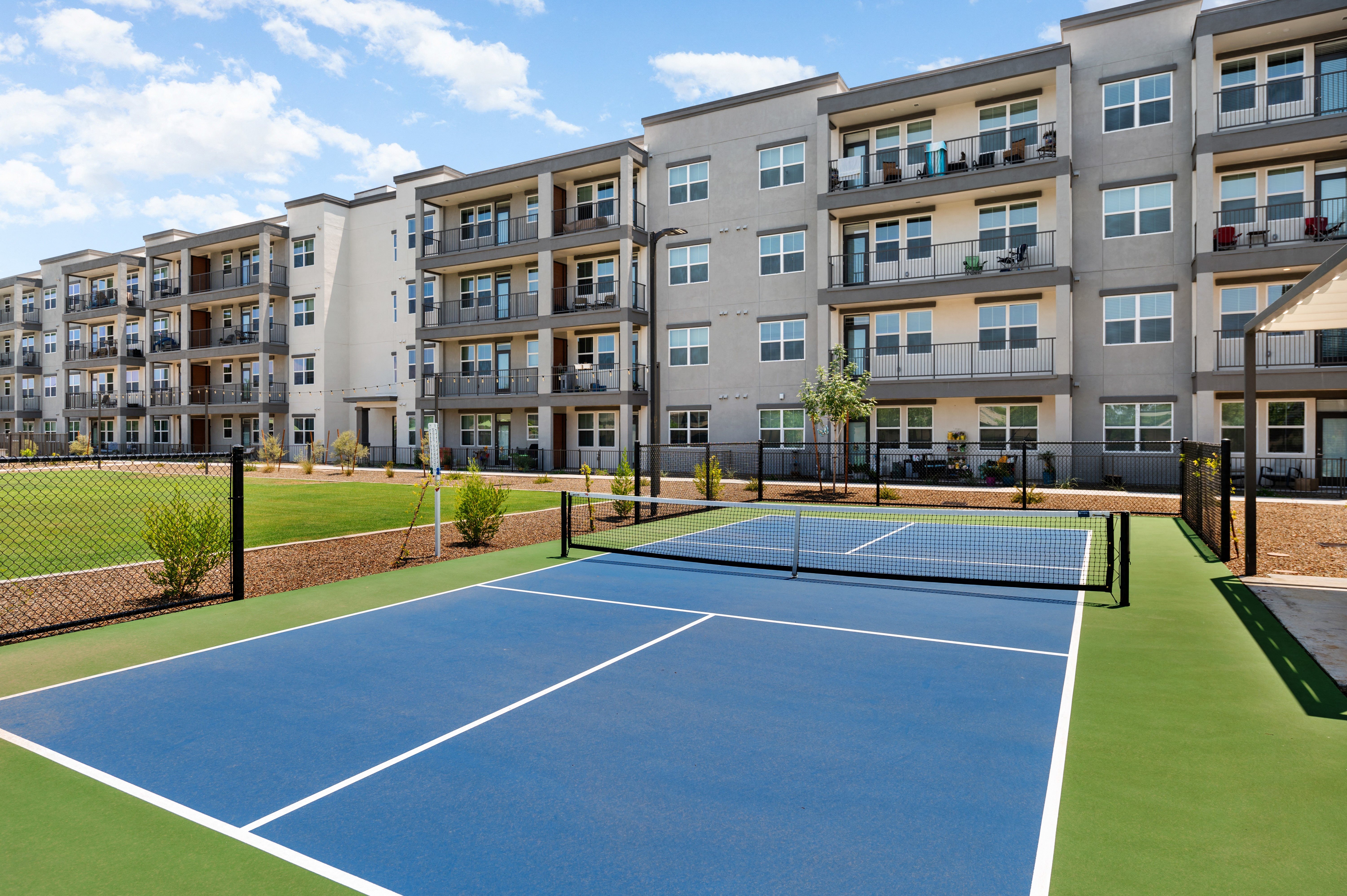an outdoor tennis court with an apartment building in the background